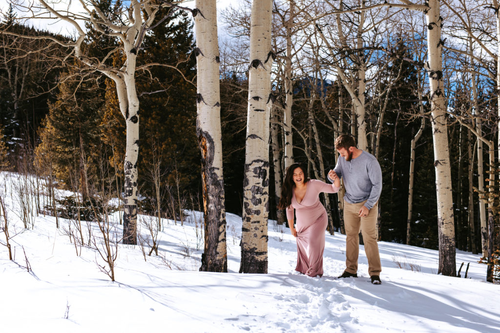 Parents to be laughing as they fall through the snow at their colorado mountain maternity session 