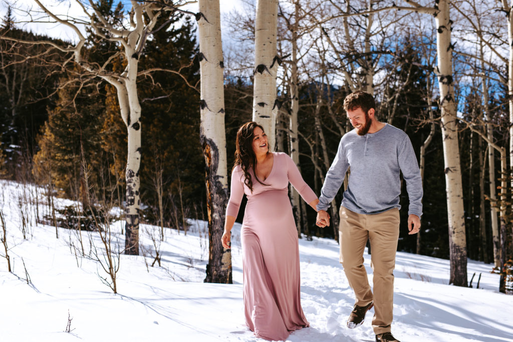 Parents to be walking in the snow at their colorado mountain maternity session 