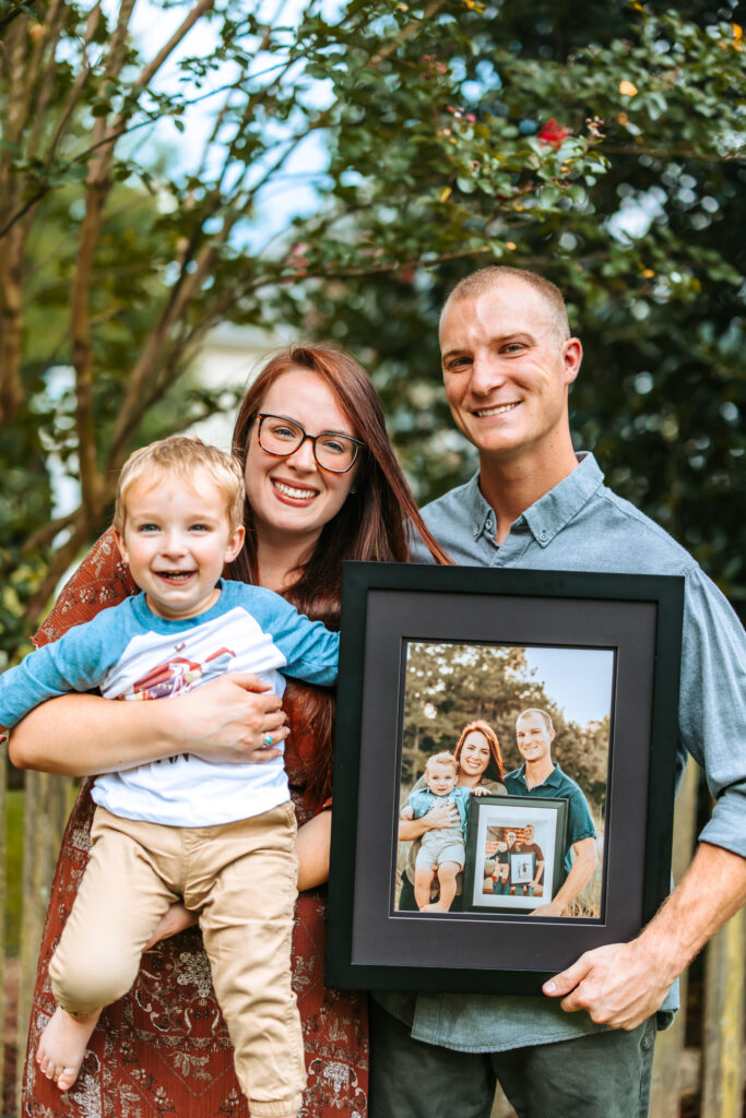 Family of three holding years past family photos in a frame, at home family photos session in High Points, North Carolina 