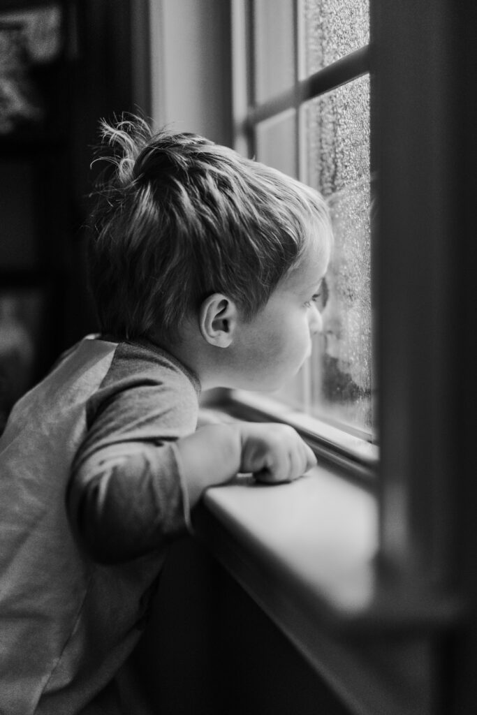 Little boy watching the rain through a window, at an in home family photos session in High Points, North Carolina 