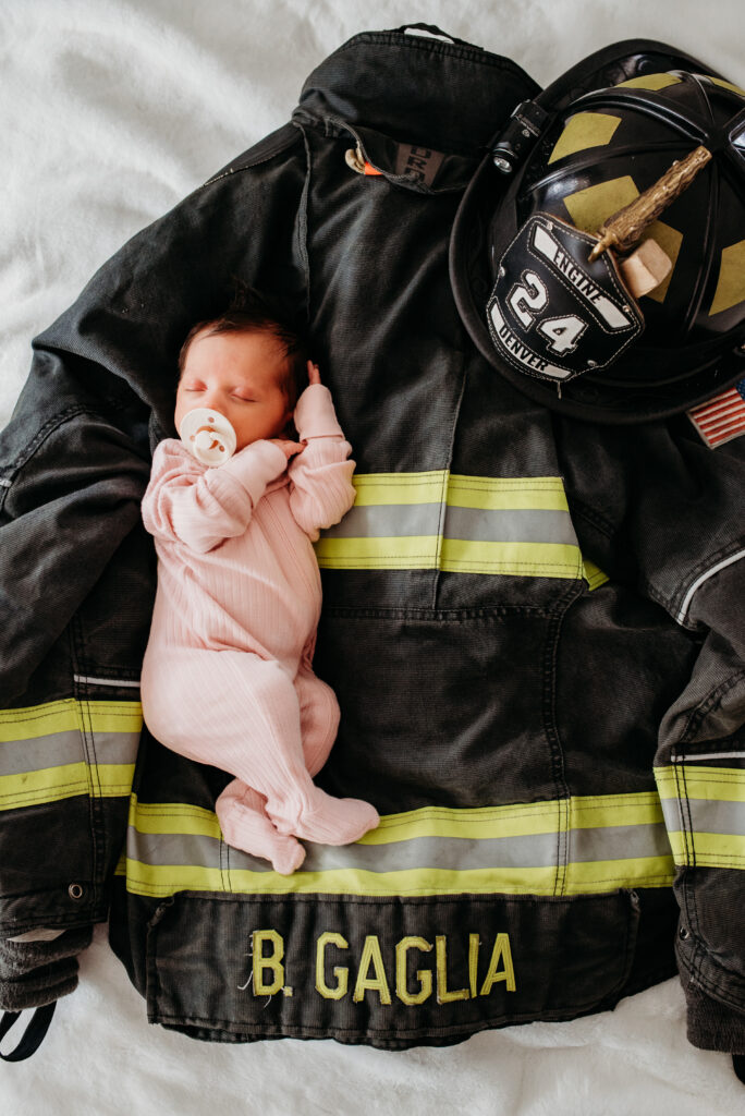 Baby girl on dads fire uniform for their in home newborn session 