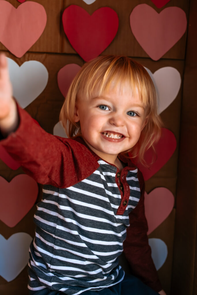 Toddler boy in a cardboard box themed for DIY Valentine's Day photos 