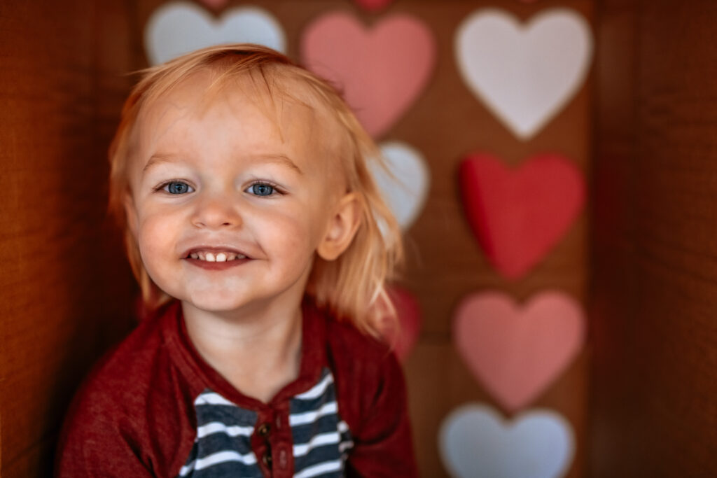 Toddler boy in a cardboard box themed with Colored Hearts for Valentines Day 