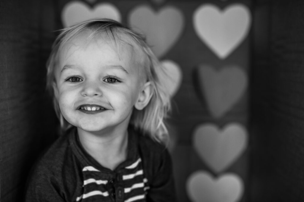 Toddler boy in a cardboard box themed with Hearts for Valentines Day Captured in Black and white 