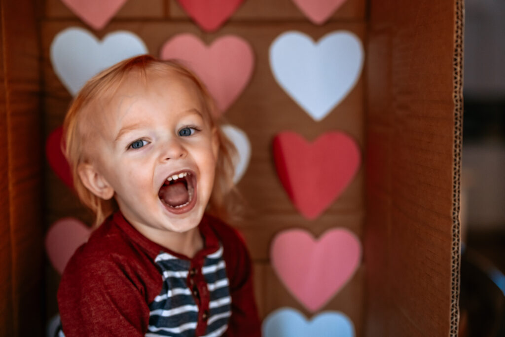 Toddler boy in a cardboard box themed with Colored Hearts for Valentines Day Laughing 