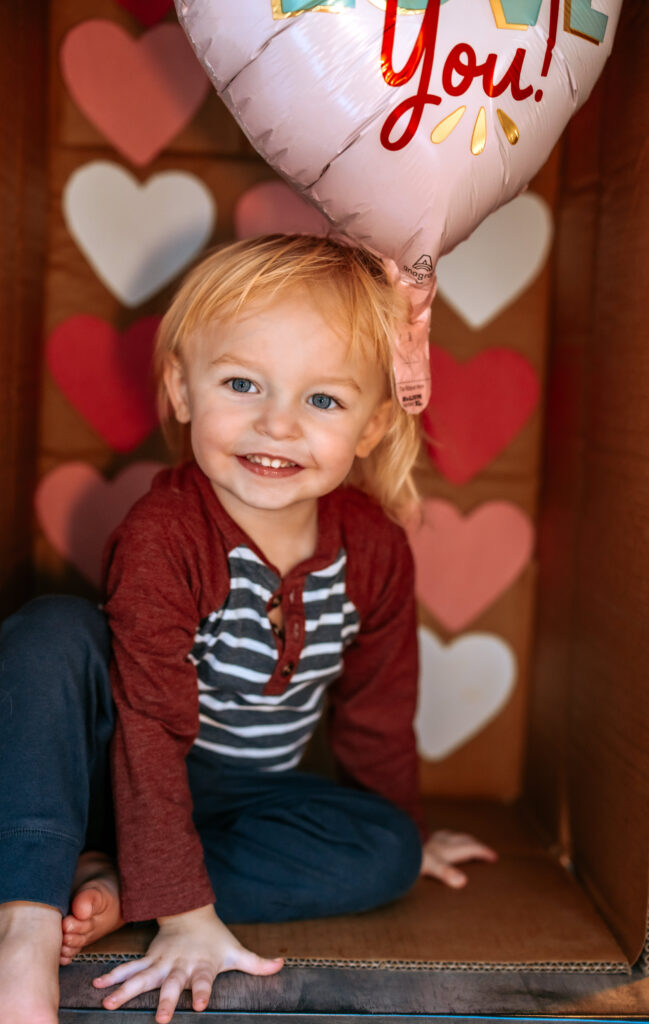 Toddler boy in a cardboard box themed for Valentines Day Photos with RattTrap Artistry for DIY Fun Photo idea 